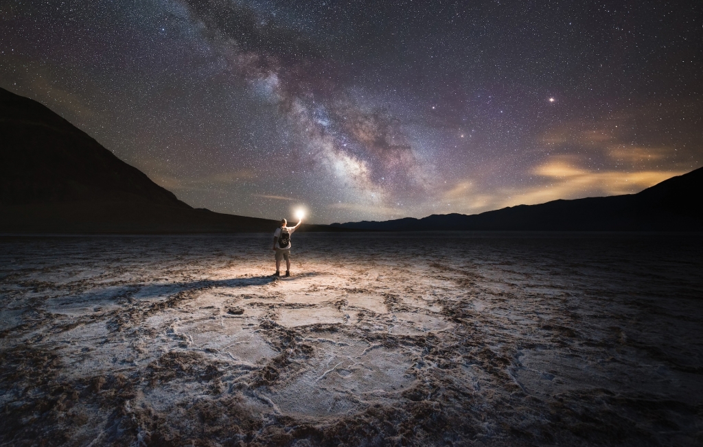 Man lighting up Badwater Basin at night under the milky way galaxy